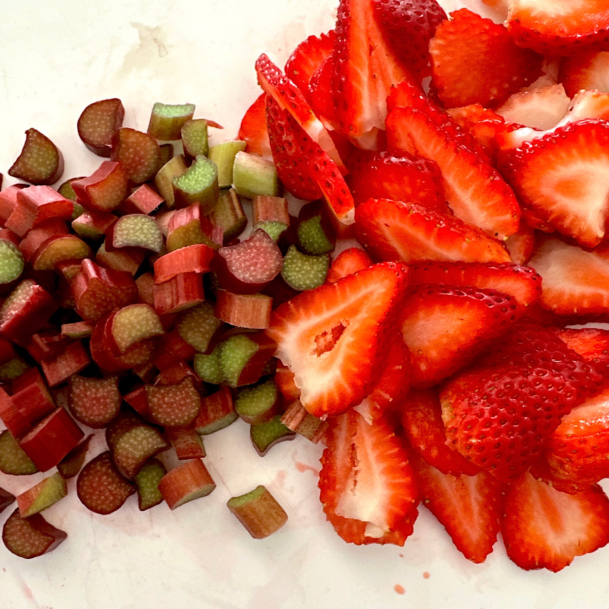 Chopped rhubarb and sliced strawberries on white cutting board.