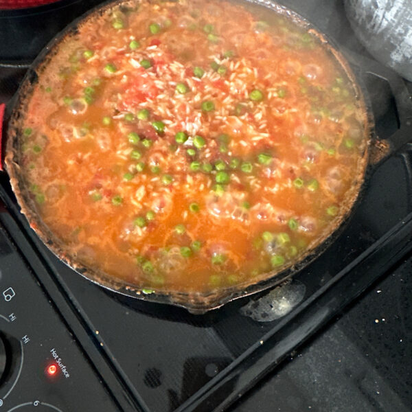 Skillet of Mexican rice with tomatoes and peas simmering on the stove.