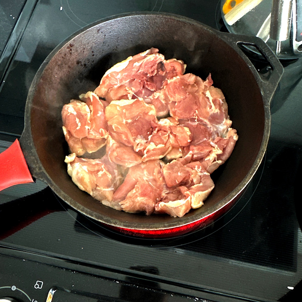 Chicken thighs in a pan on the stovetop.