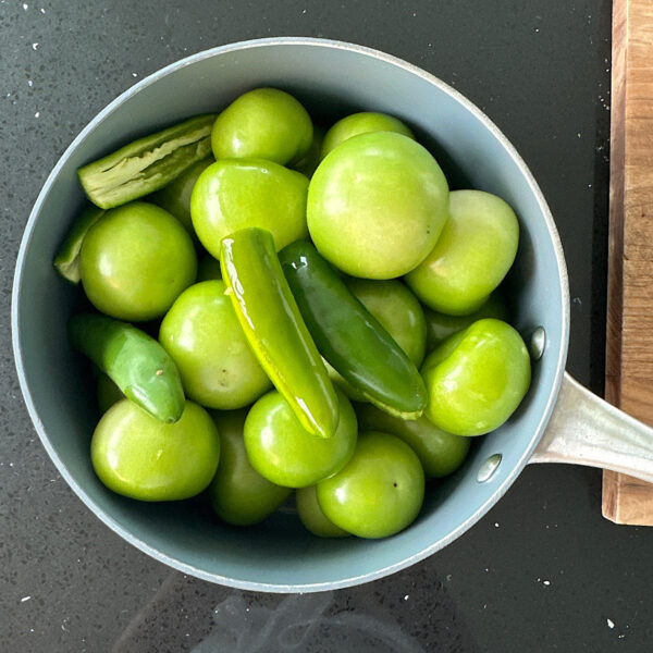 Tomatillos and serrano peppers in a pot of wate on stovetop..