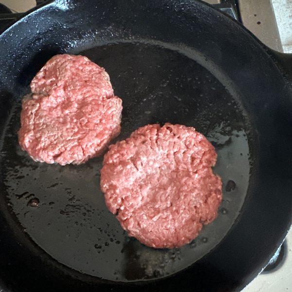 1/2 pound burger patties cooking in cast iron skillet
