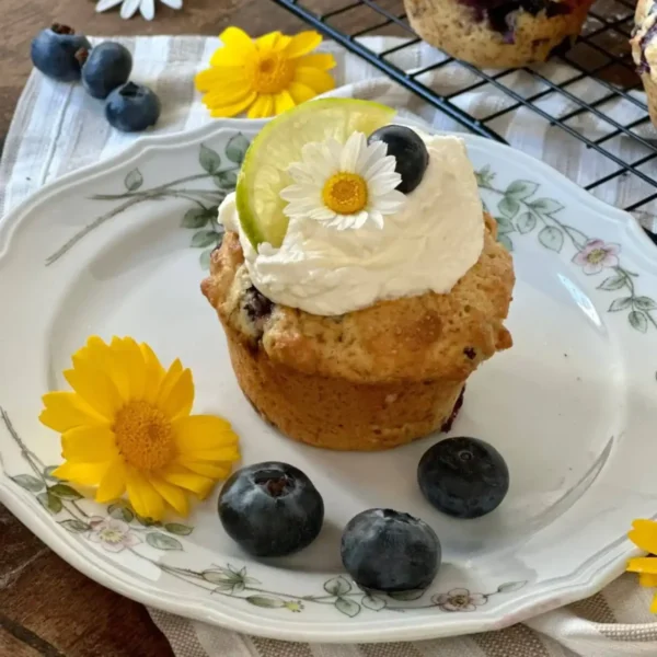 Blueberry Lime Ginger muffin on a plate with daisies as garnishes.