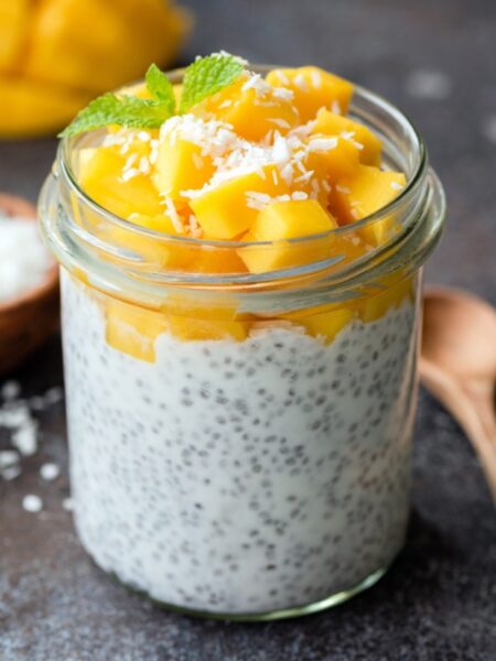Jar of chai pudding with mango on top and sprinkled with coconut.
