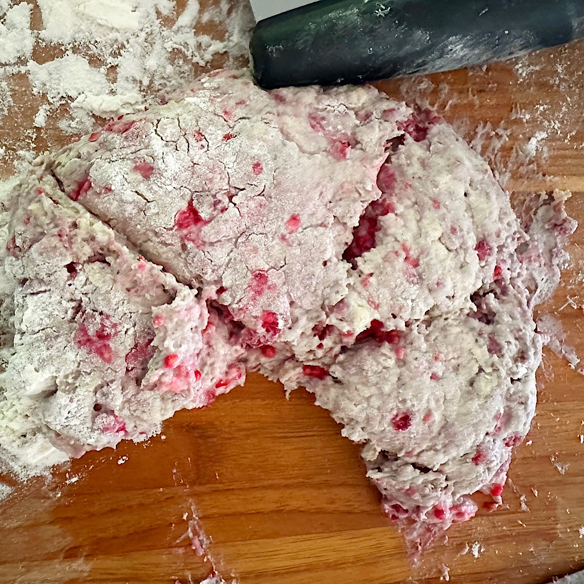 Raspberry scone dough on a cutting board cut into wedges.
