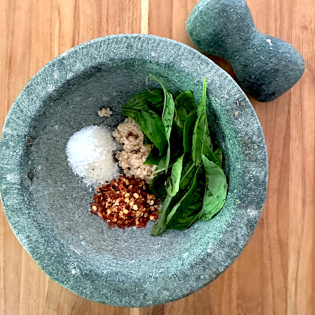 Red peppers, salt, garlic and basil leaves in a mortar and pestle