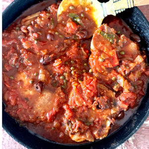 Pork chops in a skillet smothered with puttanesca sauce.