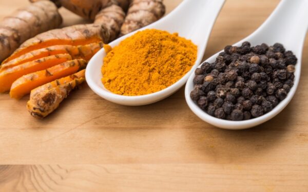 Spoons of powdered turmeric and black peppercorns.