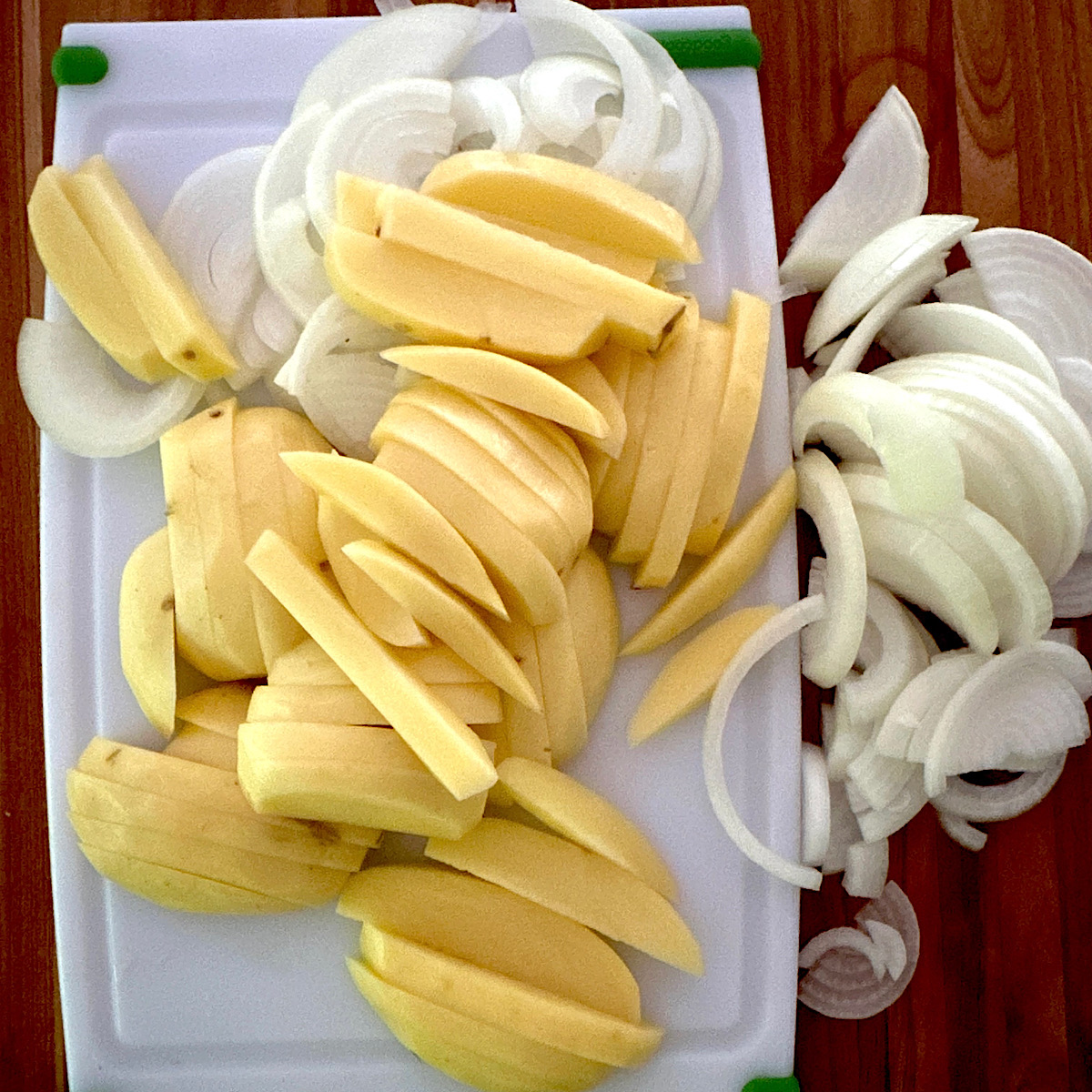 Sliced russet potatoes and sliced onion on a cutting board.