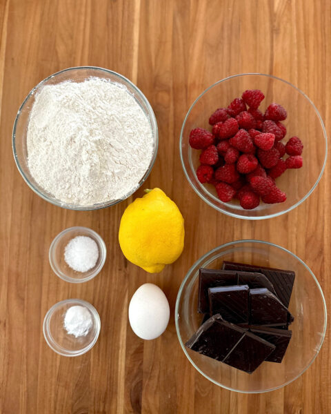 Ingredients for raspberry chocolate cookies: flour, raspberries, dark chocolate, egg,baking soda,sugar, lemon.