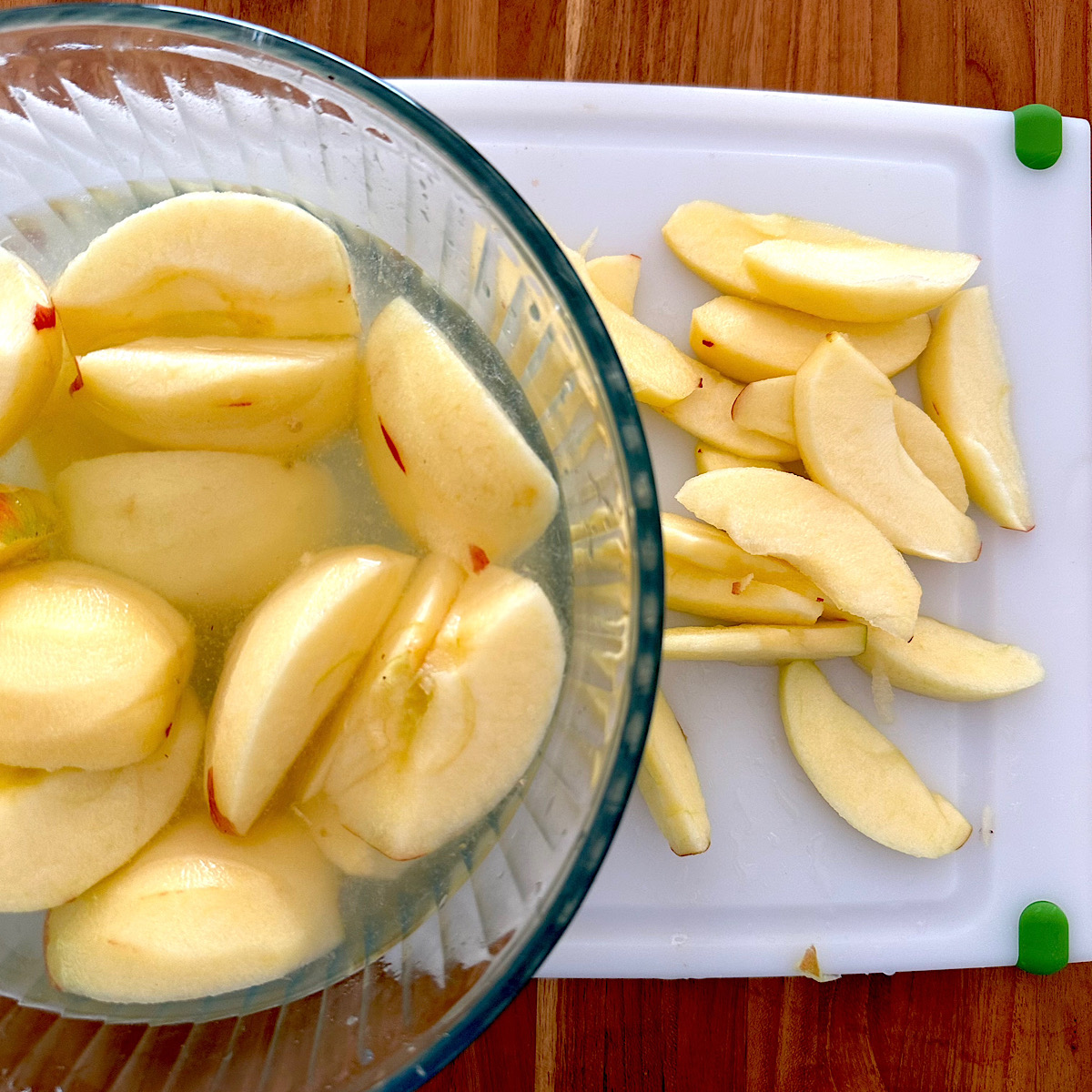 Sliced apples next to quartered apples in a bowl of lemon water