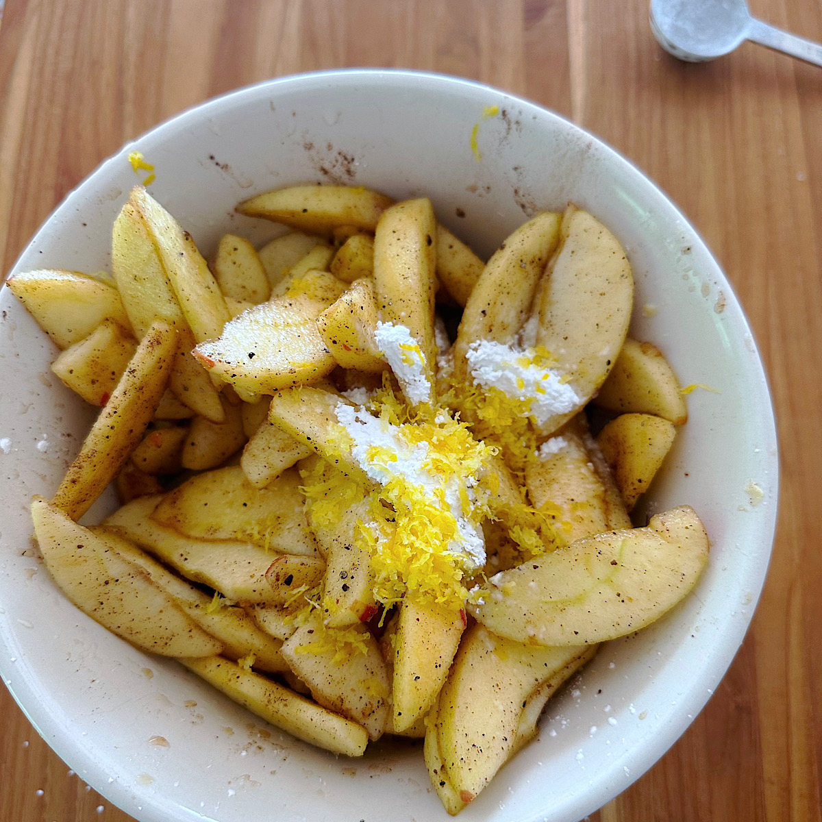 Sliced apples with spices, cornstarch and lemon zest added to the bowl.