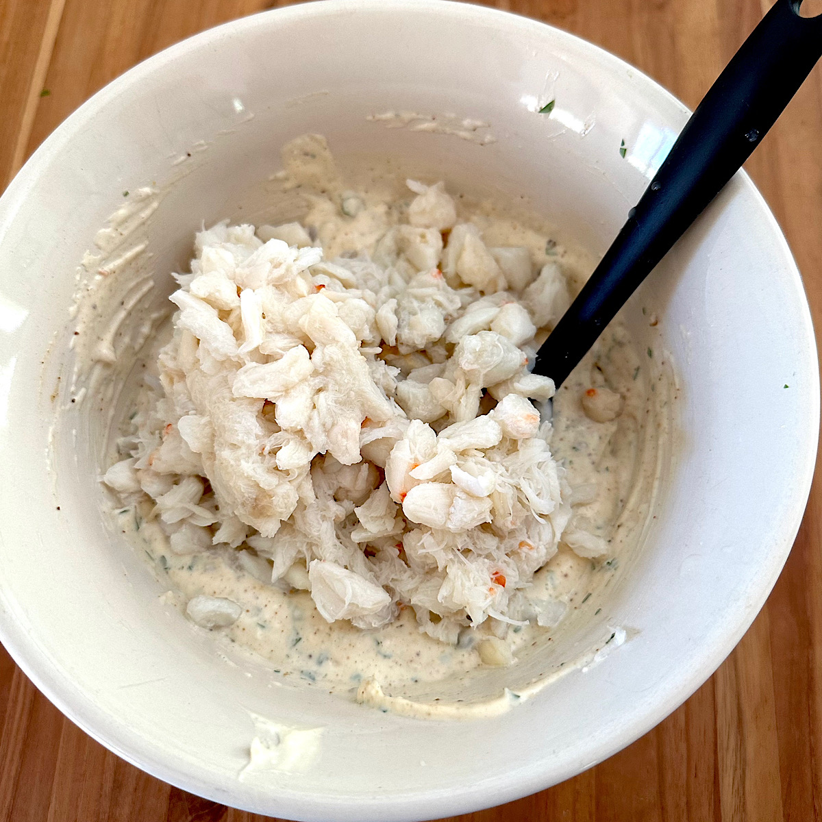 Crab salad (remoulade) in a white bowl with black spatula.