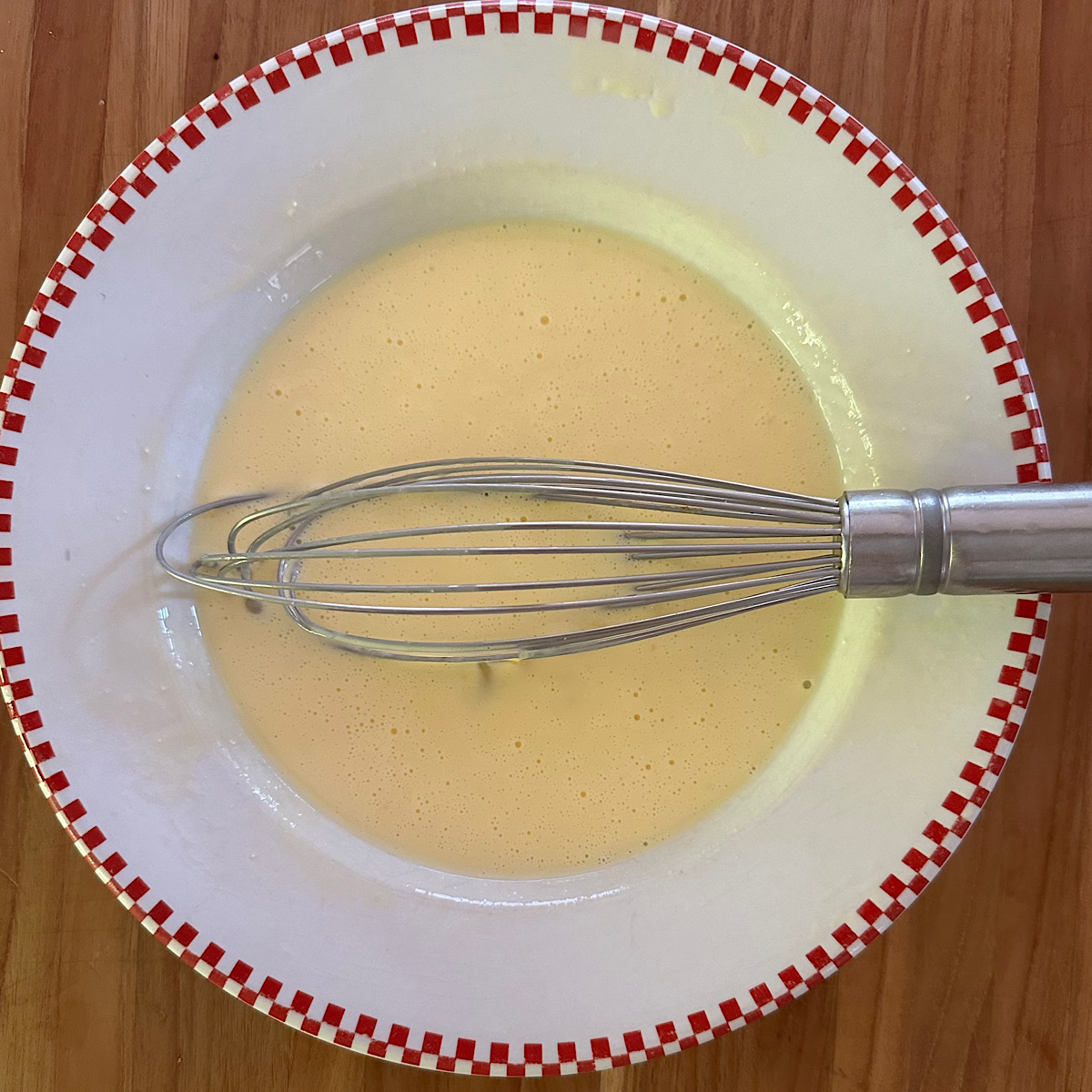 Eggs and sour cream with a wire whisk in a bowl.