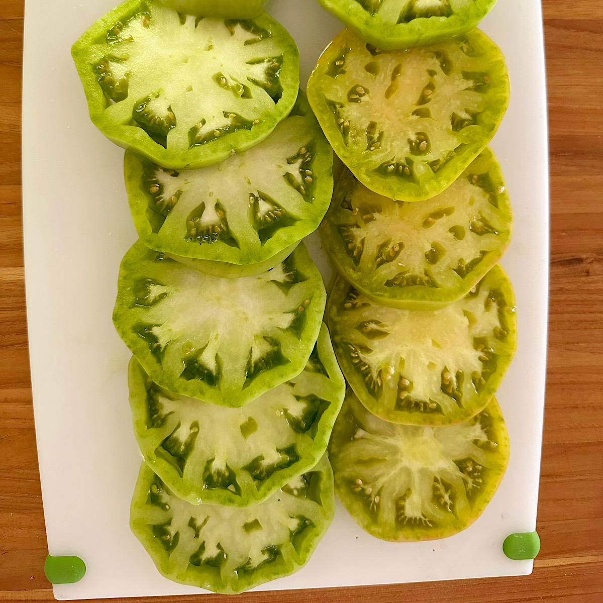 Green tomatoes sliced and layered on white board.