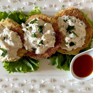 3 fried green tomatoes topped with crab salad on a bed of lettuce.