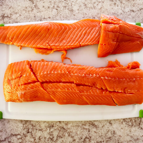 Salmon cut into several filets on a white cutting board.