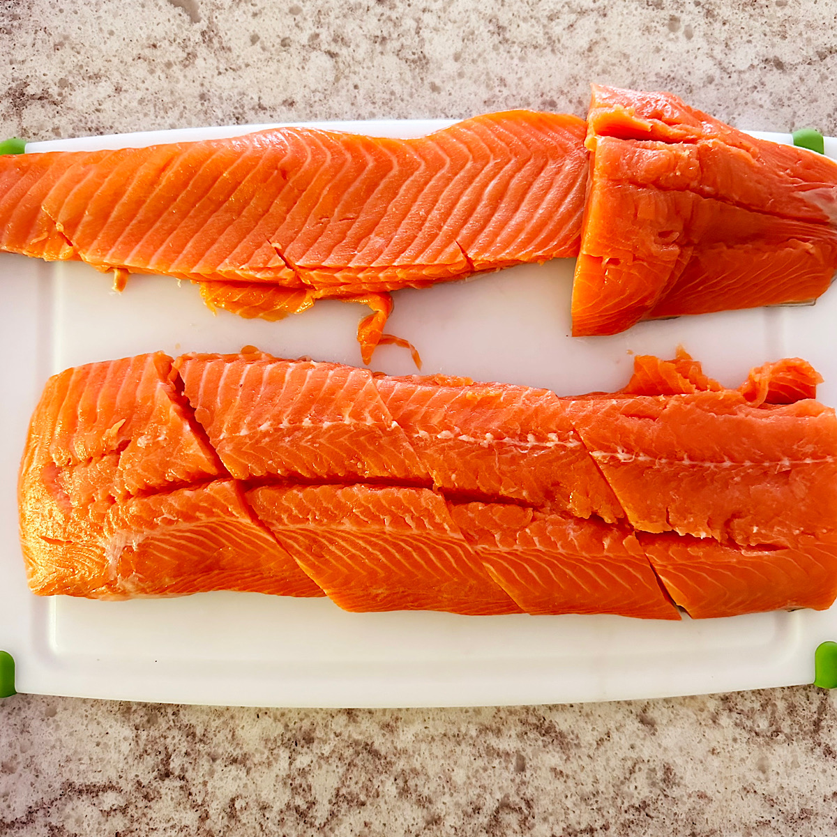 Salmon cut into several filets on a white cutting board.