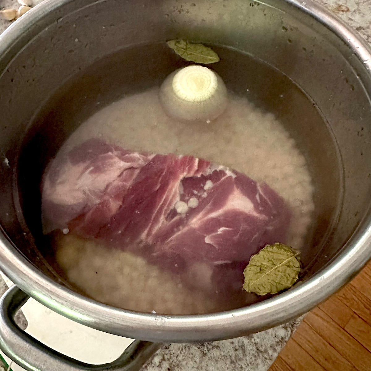 Pork butt, onions, bay leaves and hominy in pot of water