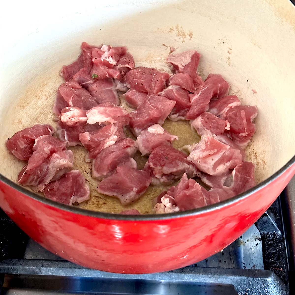 Pork pieces searing in oil in large pot.