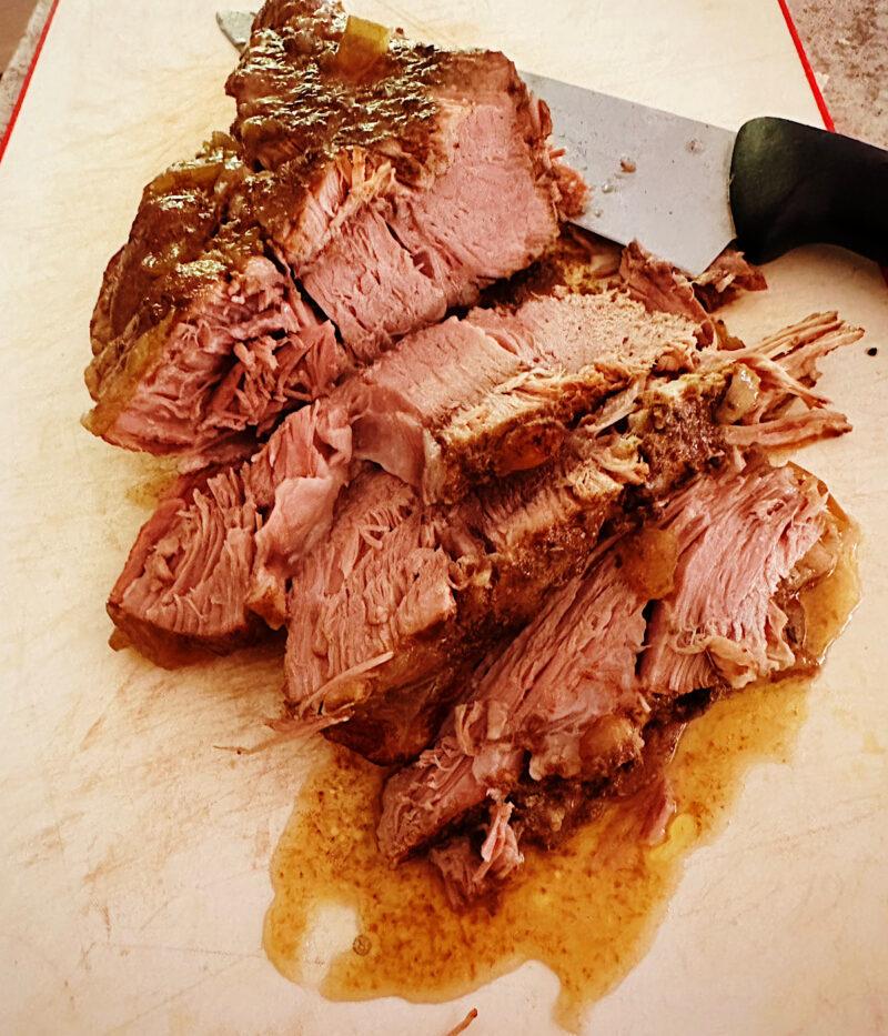 Slow cooked pork butt sliced on a cutting board.