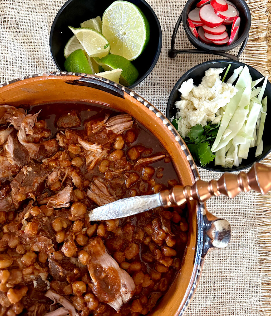 Pork pozole with side garnishes of limes, radishes, cabbage and cheese