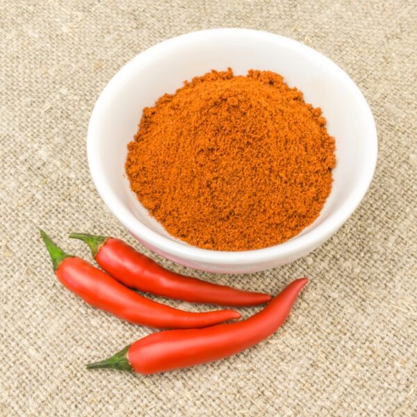 Cayenne powdered pepper in a bowl with fresh peppers on the side.