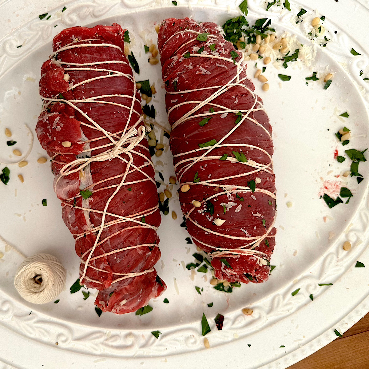 2 braciole rolls secured with twine on a white plate.