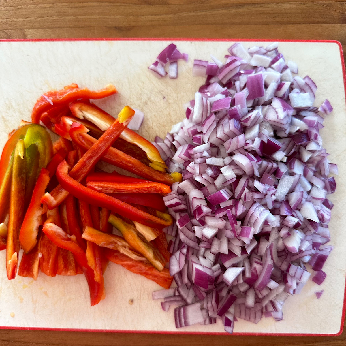 Chopped purple onion and sliced red bell pepper on cutting board.