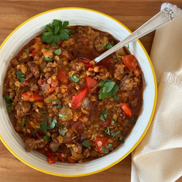 Lentil and chorizo stew in a bowl with spoon and napkin on side.