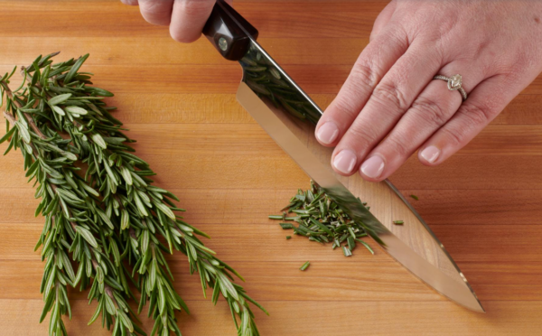 Photo of woman's hands using a large knife to chop herbs on a cutting board