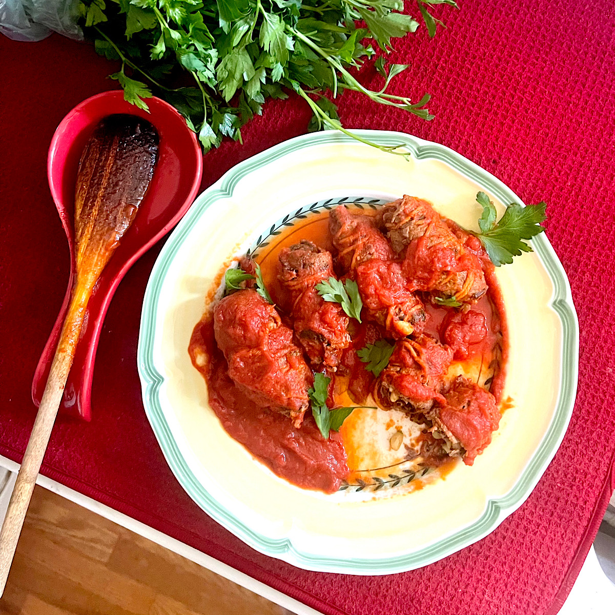 5 braciola smothered in tomato sauce on a plate with parsley in the background.