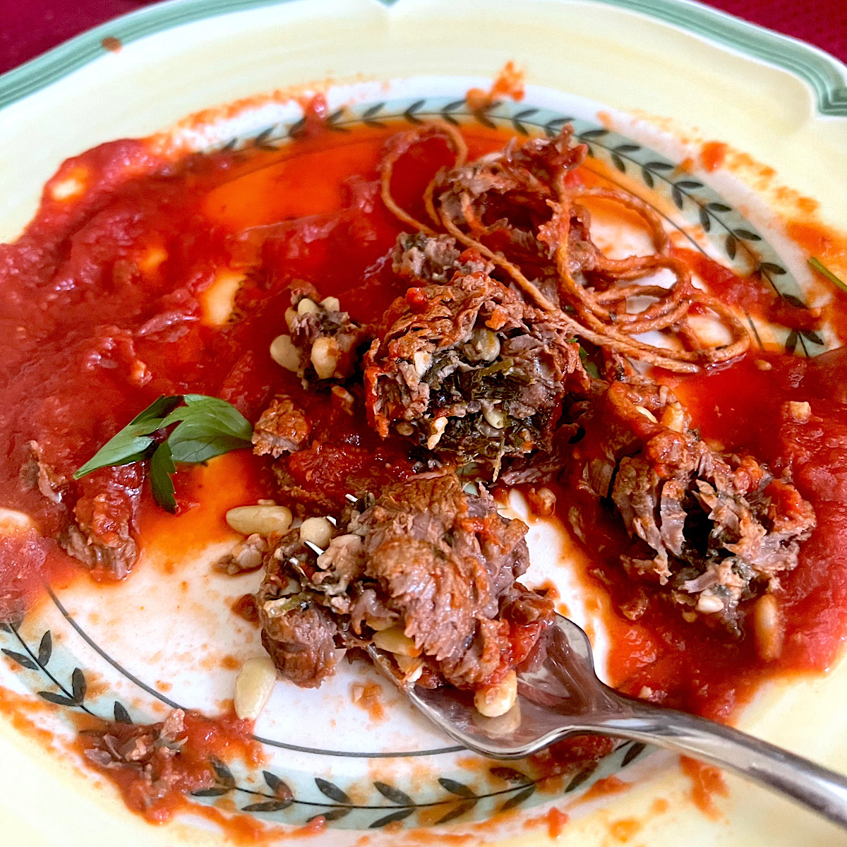 Italian braciole with tomato sauce and a slice of it on a fork.