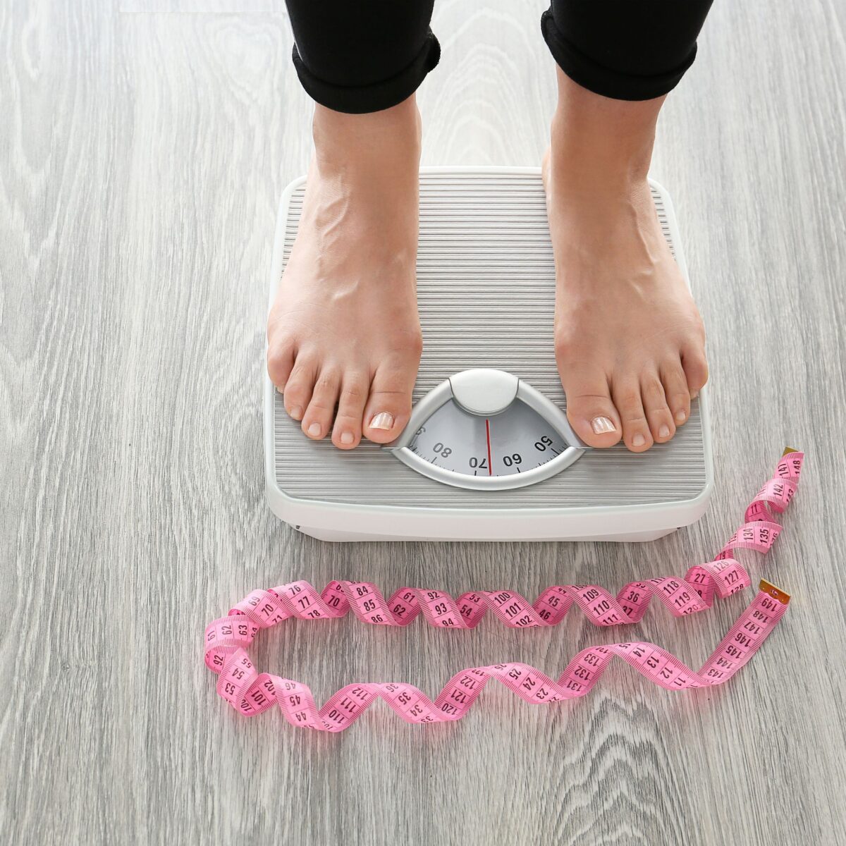 Woman weighing in on a scale with a pink measuring tape in front.