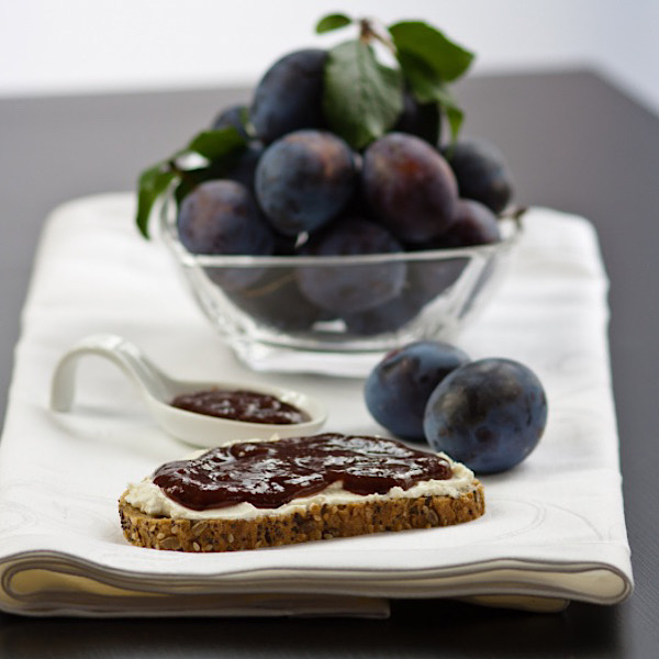 Plum butter spread on toast with Damson plums in a bowl and on the table.
