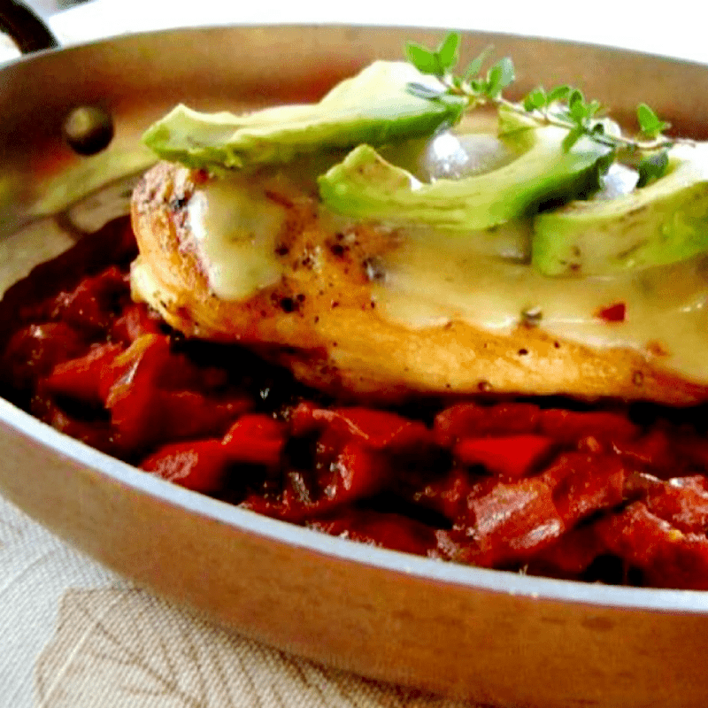Chicken on a bed of red peppers covered with cheese and avocados.