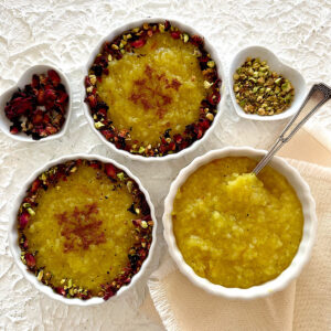 3 bowls of saffron rice pudding with rose petals and pistachio nuts on the side