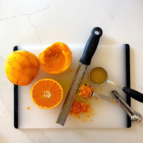 cutting board with orange cut in half, orange zest, microblade and orange juice