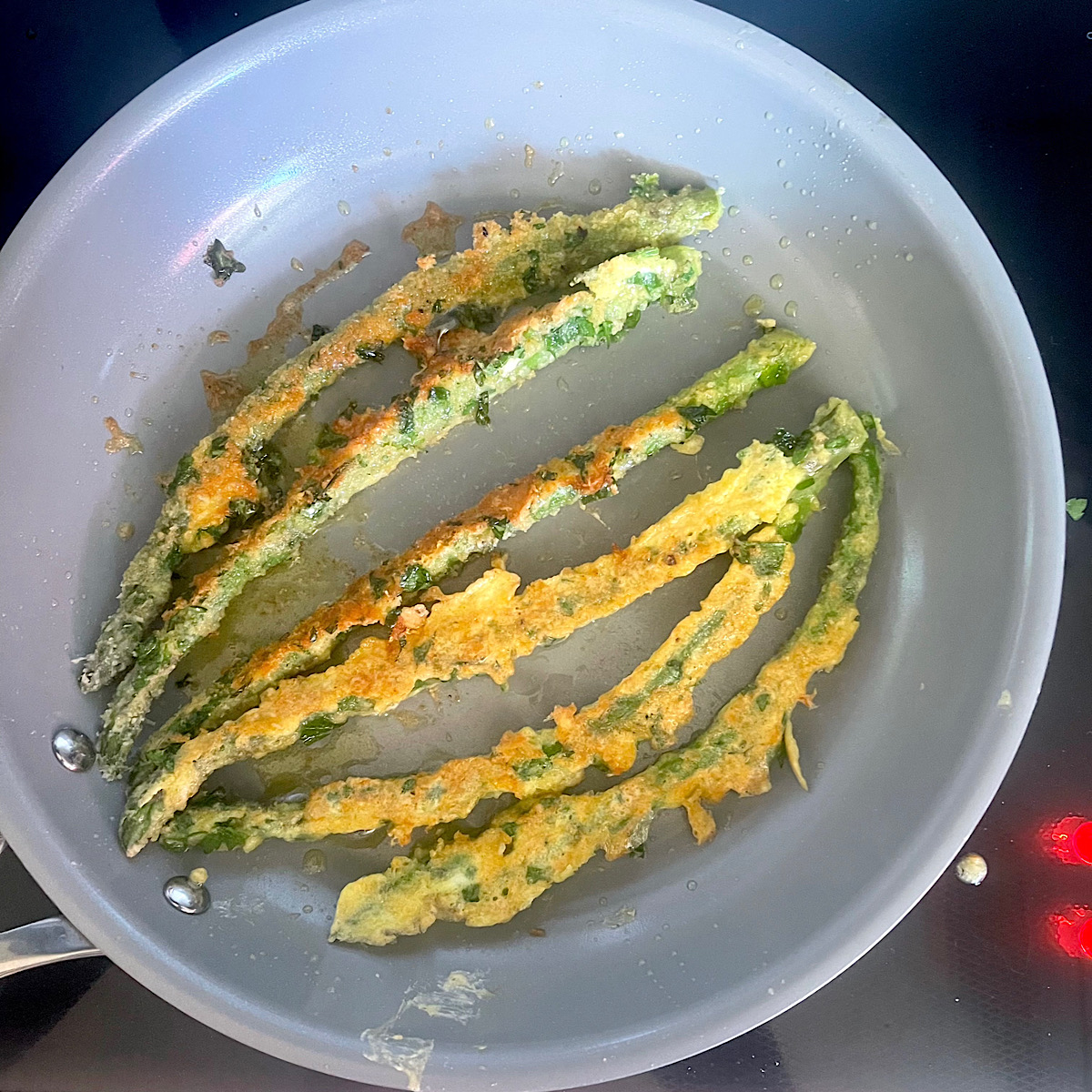 Fresh asparagus spears in a batter fried in a pan.