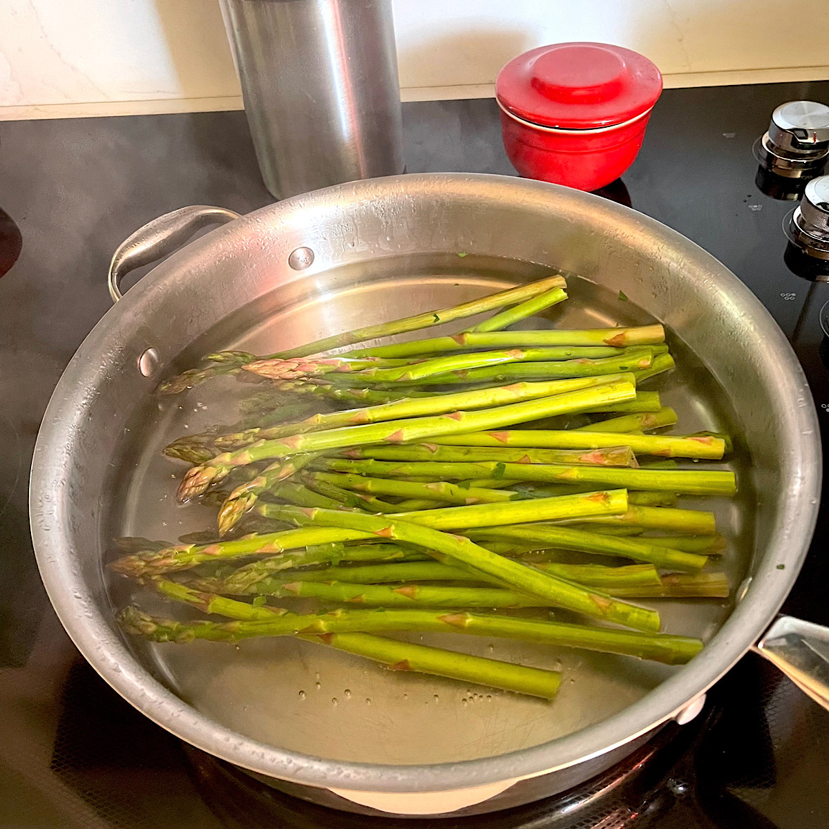 Asparagus spears parboiling in pan.