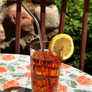 Iced tea made with rooibos (red bush) loosleaf tea blend from HeathGlen Farm. Tea is garnished with lemon slice and on an outdoor table.