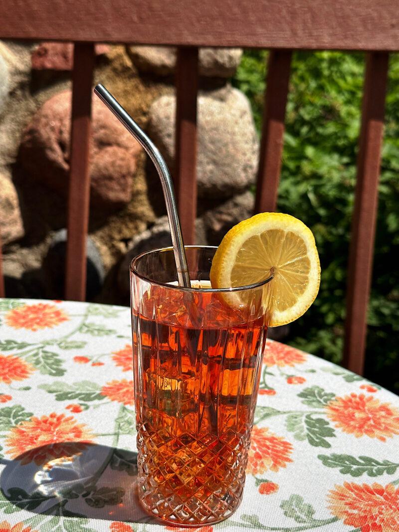 Iced tea made with rooibos (red bush) loosleaf tea blend from HeathGlen Farm. Tea is garnished with lemon slice and on an outdoor table.