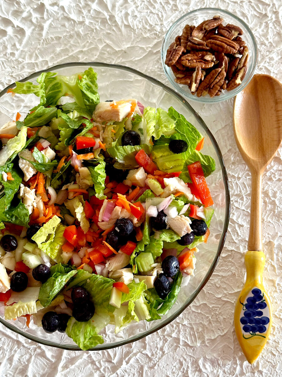 Bowl of chicken blueberry summer salad with side of walnuts