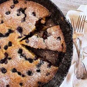 Skillet blueberry cornmeal cake with piece cut out.