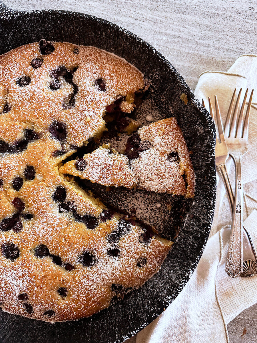 Skillet blueberry cornmeal cake with piece cut out.