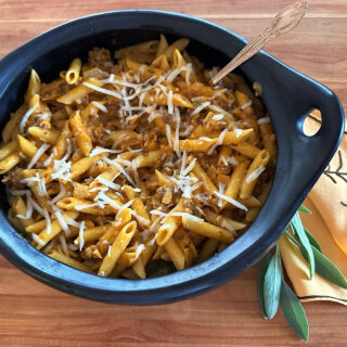 Black baking dish of penne pasta with pumpkin sausage cream sauce.