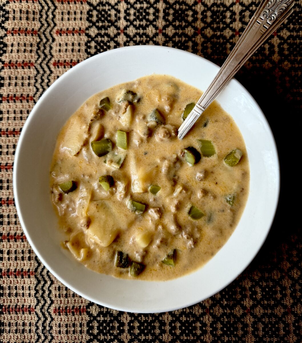Cheeseburger and pickle soup in a white bowl.