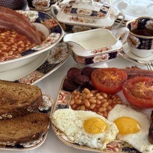 Layout of a Full English Breakfast with toast, eggs, sausage, tomatoes, baked beans and tea