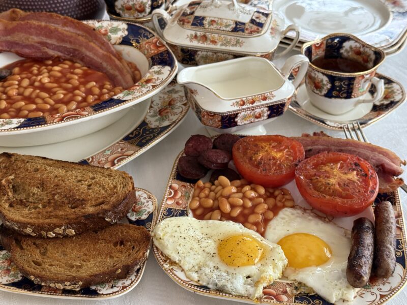 Layout of a Full English Breakfast with toast, eggs, sausage, tomatoes, baked beans and tea