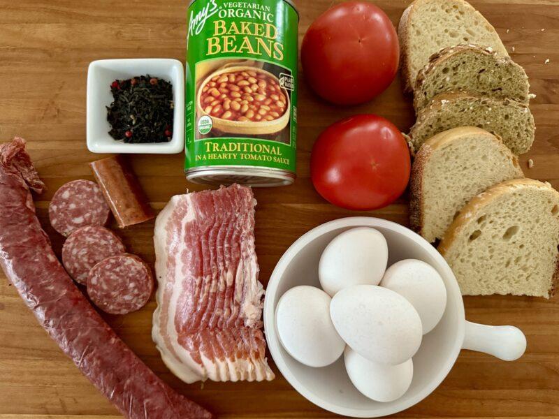 Ingredients for a Full English Breakfast with blood sausage, tea, baked beans, tomatoes, bread, eggs and bacon.