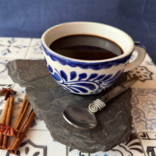 Mexican coffe (cafe de olla) on a tile platter with a side of cinnamon sticks and an arbol pepper.